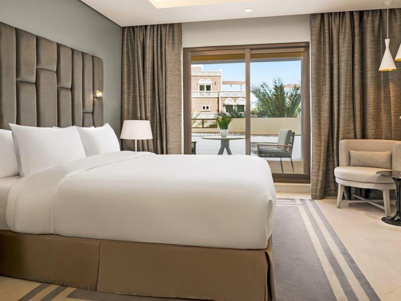 Modernes Hotelzimmer mit großem Bett, Fenster zur Terrasse und gemütlicher Sitzgelegenheit.