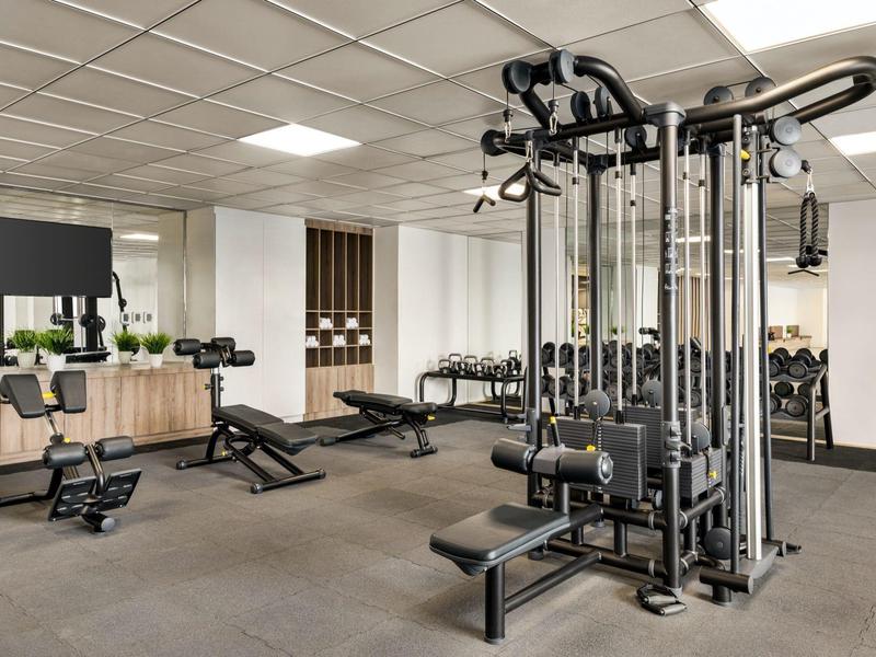Moderne Hotel-Fitnessraum mit Multifunktionsgerät, Hanteln und Trainingsbänken.