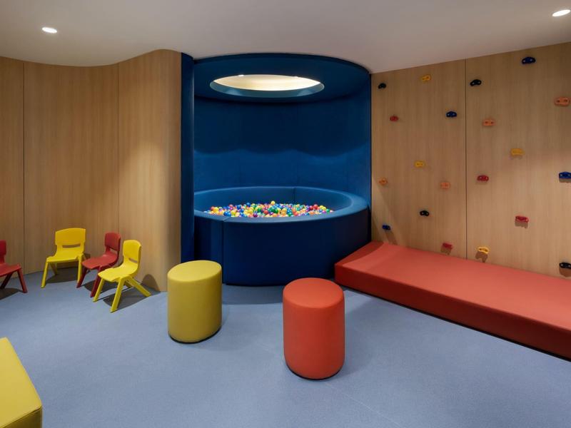 Kinderspielecke mit Kletterwand, bunten Stühlen und Bällen in einem Hotel.