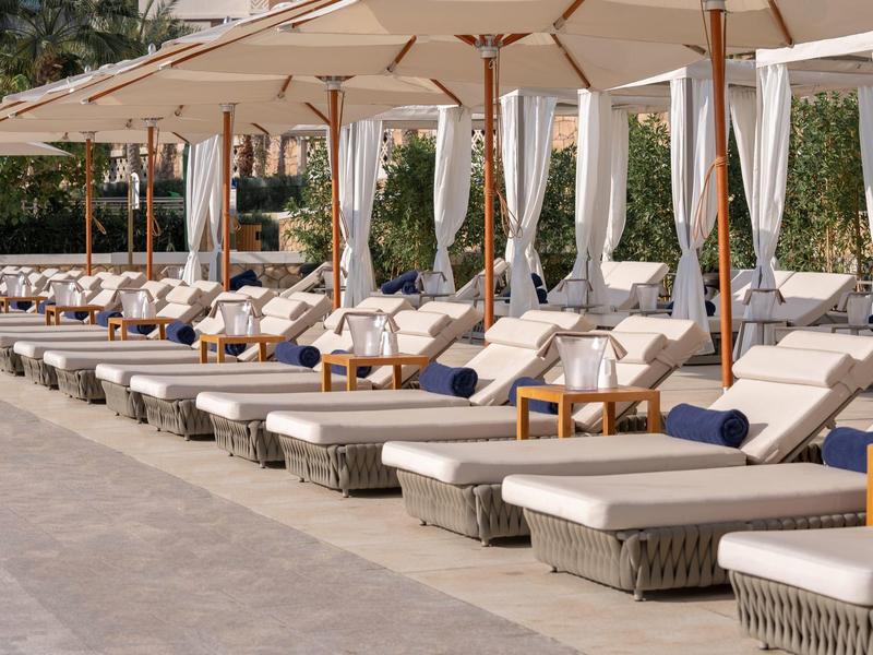 Reihe von Liegestühlen mit weißen Polstern und Sonnenschirmen neben einem Pool.