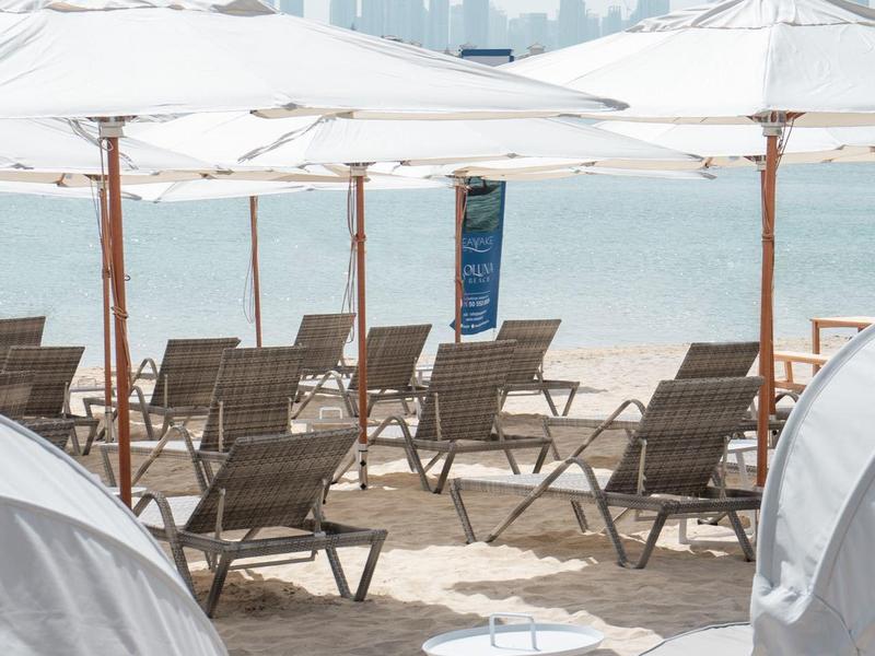 Strand mit weißen Sonnenschirmen, Liegestühlen und Blick auf die Skyline einer Stadt am Meer.