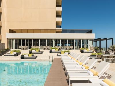 Moderner Hotelpool mit Liegestühlen und klar blauem Himmel an einem sonnigen Tag.