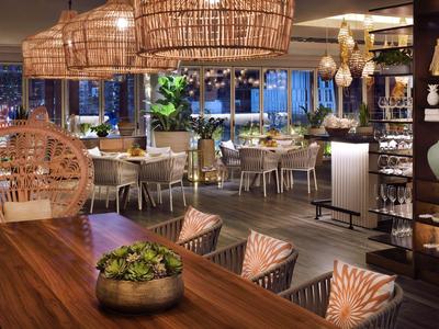 Modernes Restaurantinterieur mit Holztischen, Korblampen und dekorativen Pflanzen.