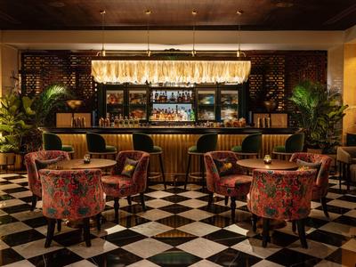 Gezellige bar met zwart-witte vleugenvloer, bloemenstoelen, houten planken en warm licht.