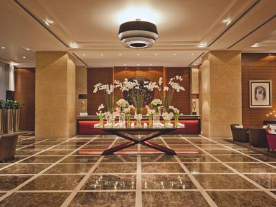 Elegante hotel lobby met marmeren vloer, centrale tafel met bloemen en warm licht.