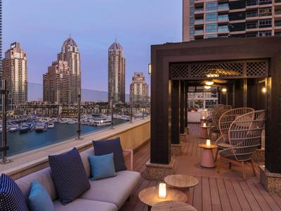 Luxe dakterraslounge met gezellige zitplaatsen, uitzicht op een jachthaven en stadssilhouet bij schemering.