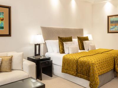 Nowoczesna sypialnia z podwójnym łóżkiem, złoto-żółtymi kołdrami i kanapą w jasnym pokoju