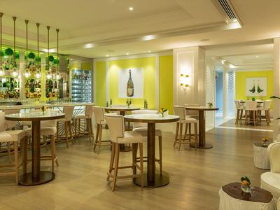 Moderne bar met houten krukken, groene accenten en warme verlichting in een hotel lounge.