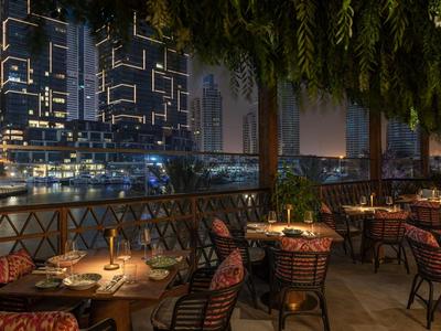 Elegantes Restaurant mit Außenbereich, gedeckten Tischen und Blick auf beleuchtete Stadt bei Nacht.