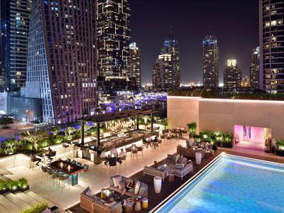 Luxuriöse Hotelterrasse mit swimmingpool und Sitzbereichen, umgeben von beleuchteten Wolkenkratzern bei Nacht.