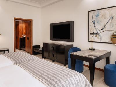 Pokój hotelowy z dwoma łóżkami, niebieskim fotelem, telewizorem i eleganckim wystrojem.