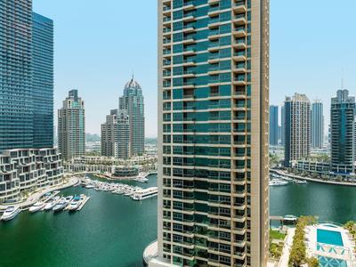 Uitzicht op de haven met jachten, hoge gebouwen en een zwembad onder een heldere lucht.