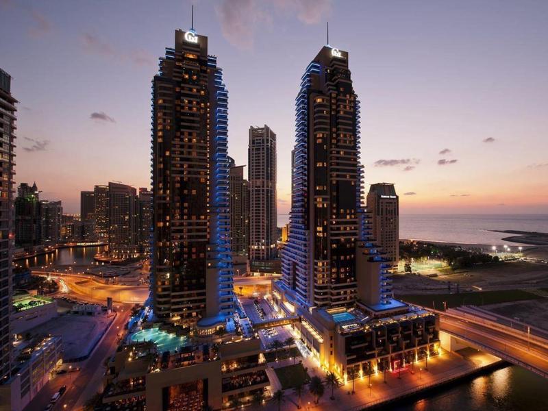 Stadsgezicht met verlichte hoge gebouwen bij schemering aan het water.