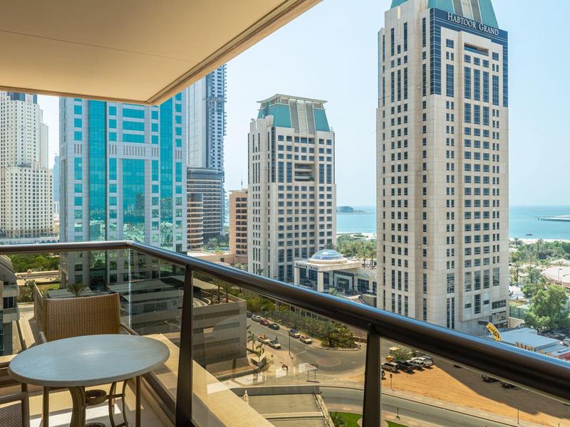 Balkon met zitgedeelte met uitzicht op hoge gebouwen en een strand in de verte.