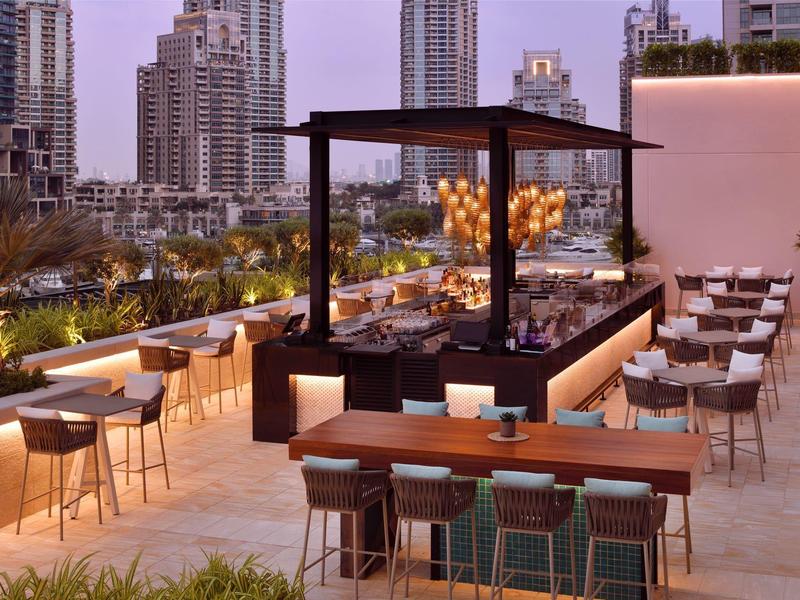 Moderne buiten eetruimte met tafels, stoelen, vuurplaats en stadsachtergrond.