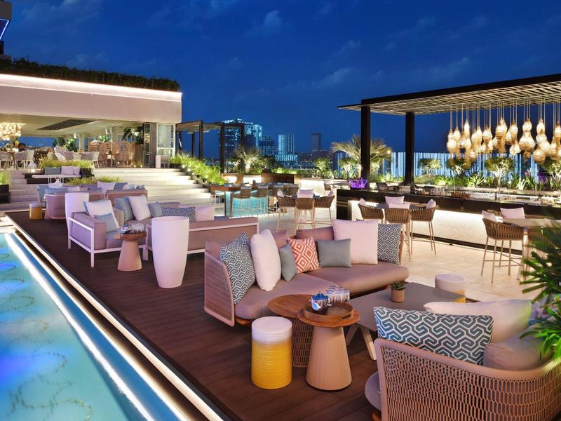 Moderne buitenlounge met zwembad, gezellige zitplaatsen en sfeerverlichting onder een nachtelijke hemel.