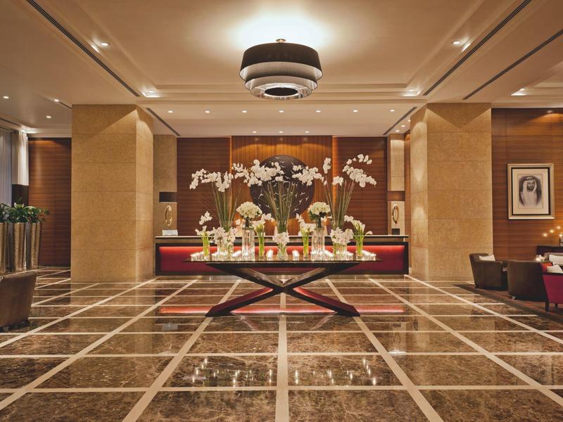 Elegante hotel lobby met marmeren vloer, centrale tafel met bloemen en warm licht.