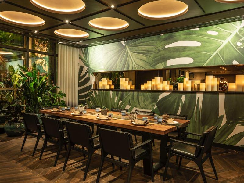 Moderne eetkamer met houten tafel, zwarte stoelen, groen bladbehang en plafondlampen.