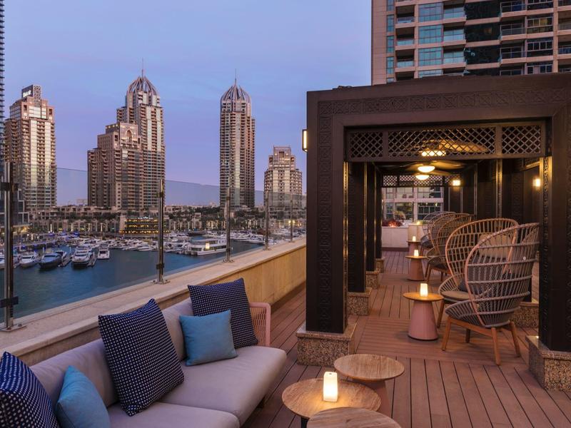 Luxe dakterraslounge met gezellige zitplaatsen, uitzicht op een jachthaven en stadssilhouet bij schemering.