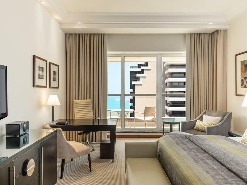 Moderne hotelkamer met bed, bureau, stoelen en balkon met uitzicht op de oceaan.