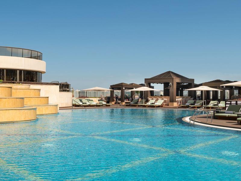 Luxe zwembad met ligstoelen en heldere blauwe lucht bij een resort.