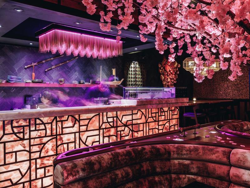 Modern hotel bar with pink lighting and blooming cherry blossoms, cozy seating areas.