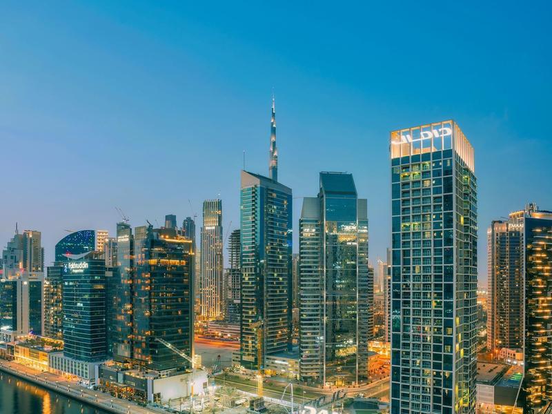 View of a modern harbor city with illuminated skyscrapers by the water at dusk.