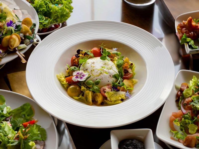A white plate with rice and vegetables surrounded by several plates of salads on a wooden table.