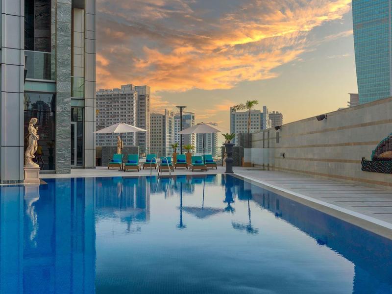Rooftop pool with blue water in front of city buildings at sunset