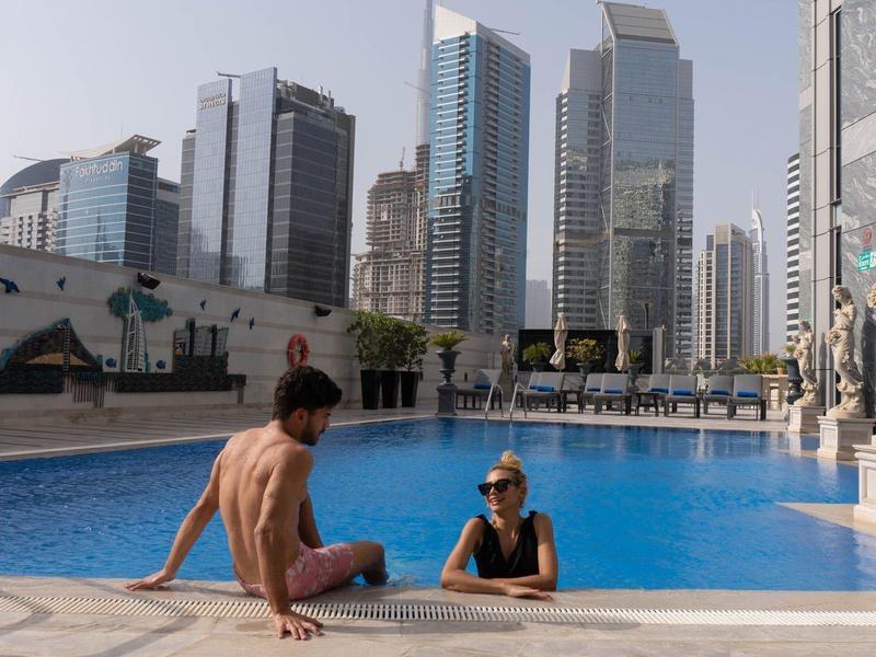 Two people relax by a pool with a view of a modern cityscape and skyscrapers.