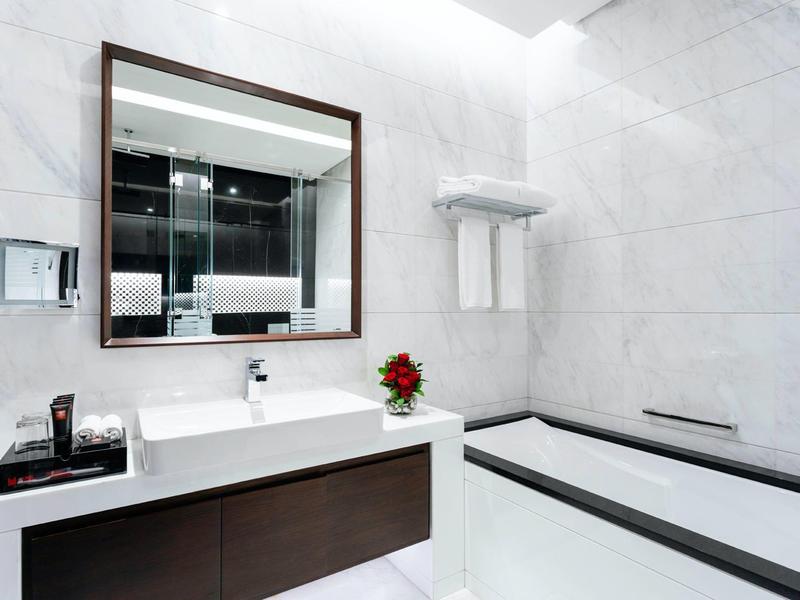 Modern bathroom with white bathtub, large mirror, and sink with dark vanity cabinet.