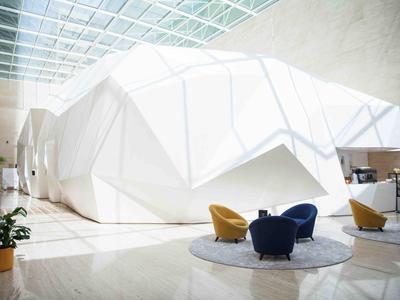 Heller Aufenthaltsraum mit weißer, geometrischer Struktur und Sitzbereichen mit bunten Stühlen.