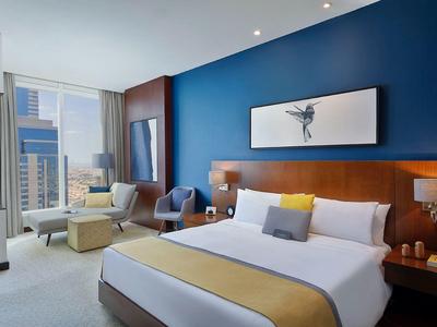 Modernes Hotelzimmer mit großem Bett, blauer Akzentwand und Blick auf die Stadt.