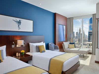 Modernes Hotelzimmer mit zwei Betten, blauem Akzentwand und Fenster mit Stadtblick.