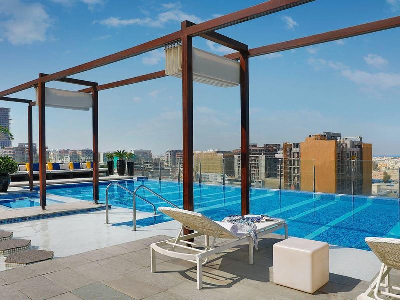 Dachpool mit Liegestühlen und Stadtblick bei sonnigem Wetter.