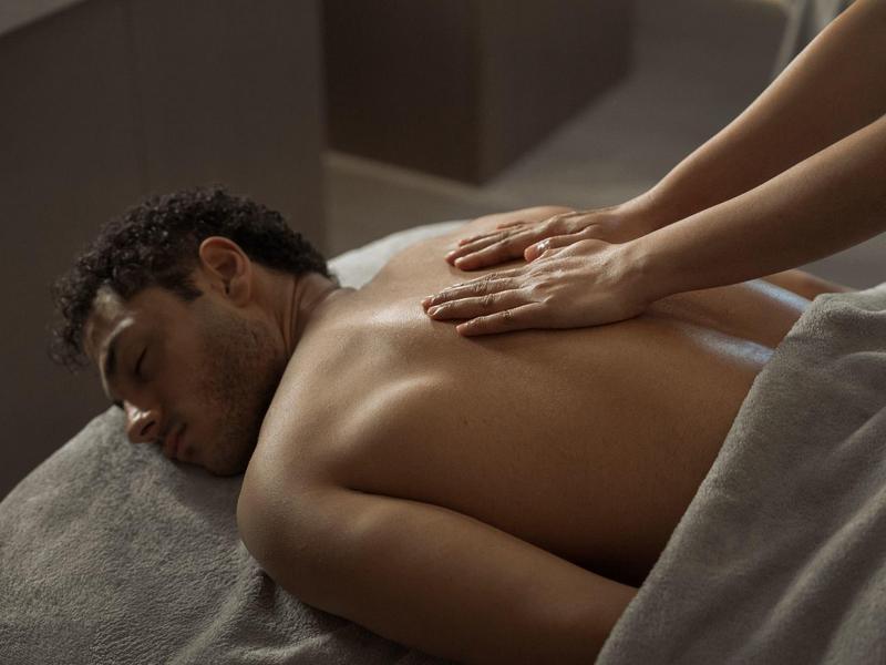 Man krijgt een rugmassage in een rustige, gedimde kamer met bruine tinten.