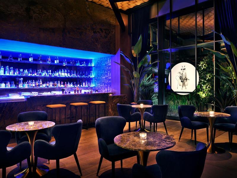 Donkere bar met blauwe verlichting, ronde tafels en comfortabele stoelen in stijlvolle omgeving.