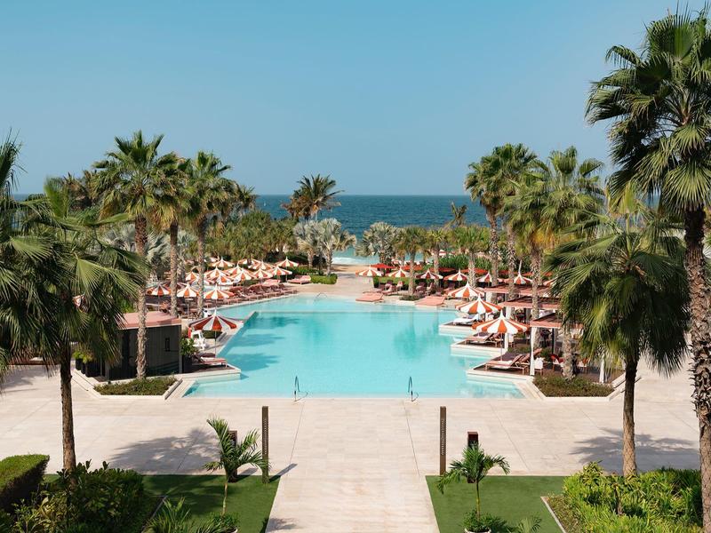 Groot zwembad met palmbomen en parasols bij zee op een zonnige dag.