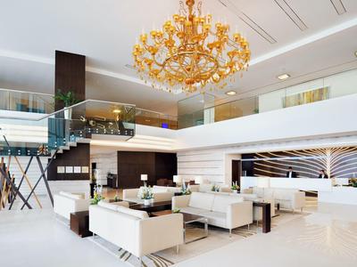 Area lounge luminosa dell'hotel con divani bianchi, lampadario dorato e design moderno.