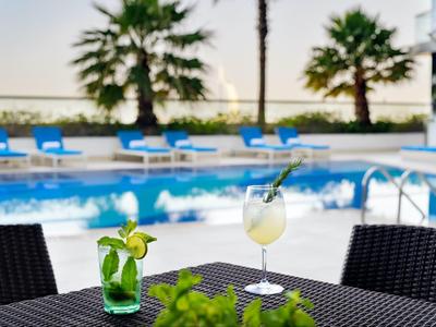 Due bevande su un tavolo con piscina e palme sullo sfondo in una giornata di sole.