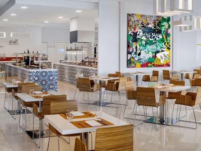 Area ristorante dell'hotel arredato con tavoli in legno, sedie e arte murale colorata.