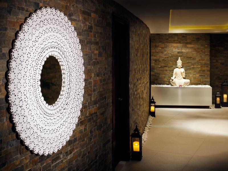 Area benessere moderna con scultura di Buddha, candele e specchio rotondo su parete in pietra.