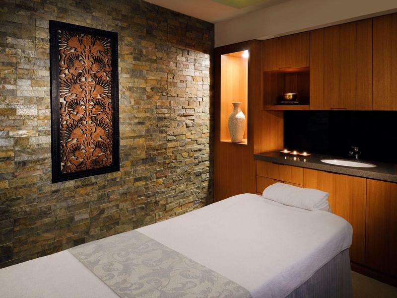 Stanza per trattamenti con lettino da massaggio, parete in pietra e decorazioni in legno caldo.