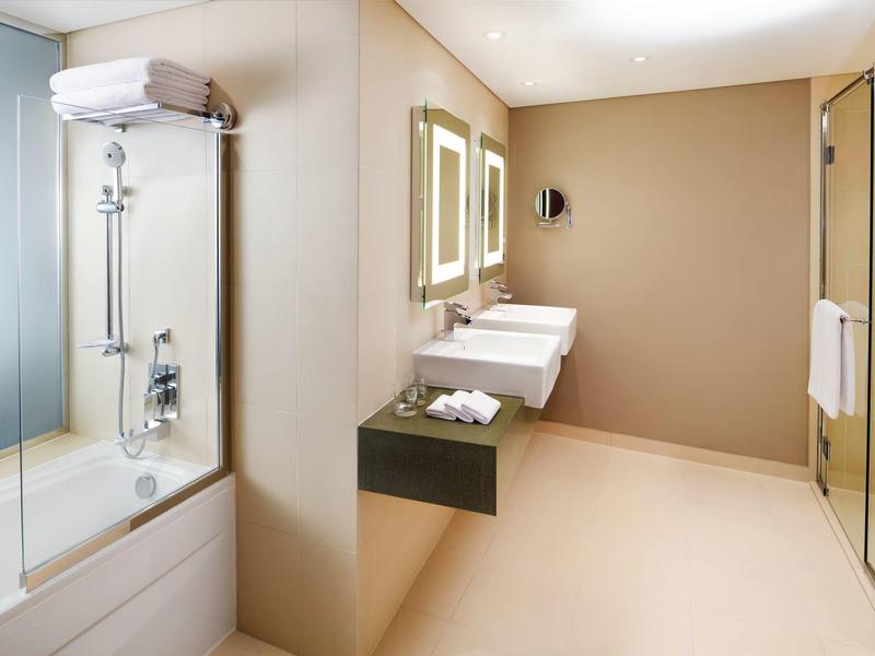 Moderno bagno d'hotel con vasca, doppio lavabo e specchi illuminati.