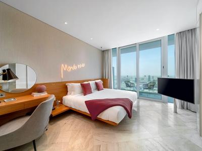 Moderní hotelový pokoj s manželskou postelí, psacím stolem, panoramatickými okny a výhledem na město.