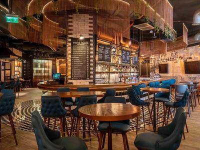 Moderní bar s dřevěným stropem, kulatými stoly a modrými židlemi.