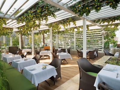 Zastřešená venkovní část restaurace s bílými ubrusy a zelenými rostlinami.