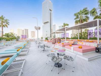 Moderne Dachterrasse mit Liegestühlen, Sitzgelegenheiten und Palmen in sonniger Stadtumgebung.