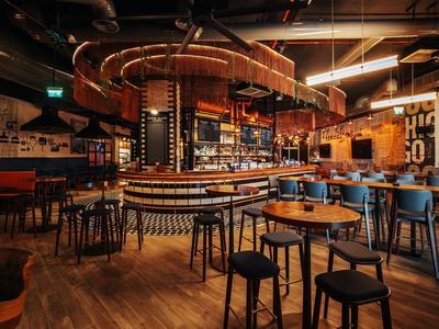 Gezellige hotelbar met ronde houten tafels, barkrukken en warm licht.