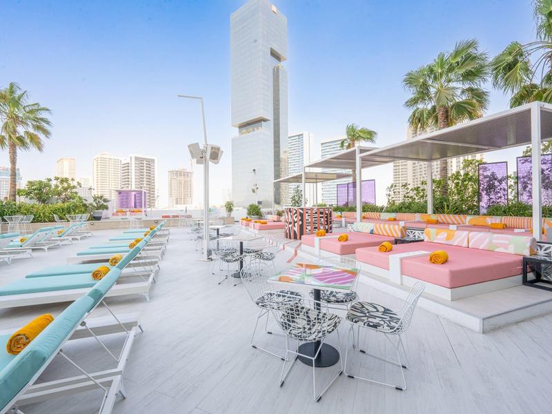 Moderne dakterras met ligstoelen, zitplaatsen en palmbomen in een zonnige stedelijke omgeving.